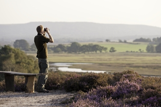 Person with binoculars looking out over a heathland landscape by Ross Hoddinott/2020VISION