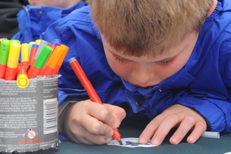 A child colouring in with a tin of coloured pens next to him by Amy Lewis
