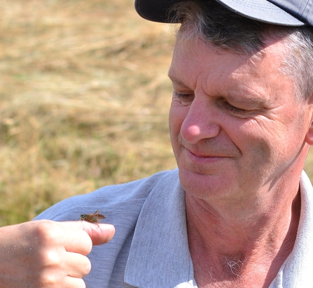 Gary Farmer - sunny day, man with a cap on smiling at a grasshopper sat on his thumb by Madi Farmer